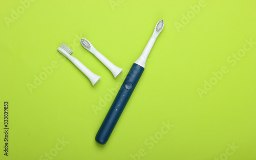 Teeth care. Modern electric toothbrush with nozzles on green background. Top view. Minimalism