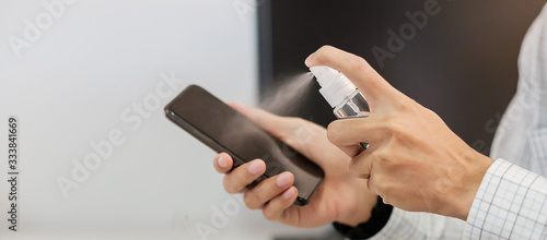 Man hand spraying alcohol sanitizer bottle to the Smartphone, against Novel coronavirus or Corona Virus Disease (Covid-19) at office or home. Antiseptic, Hygiene and Health concept
