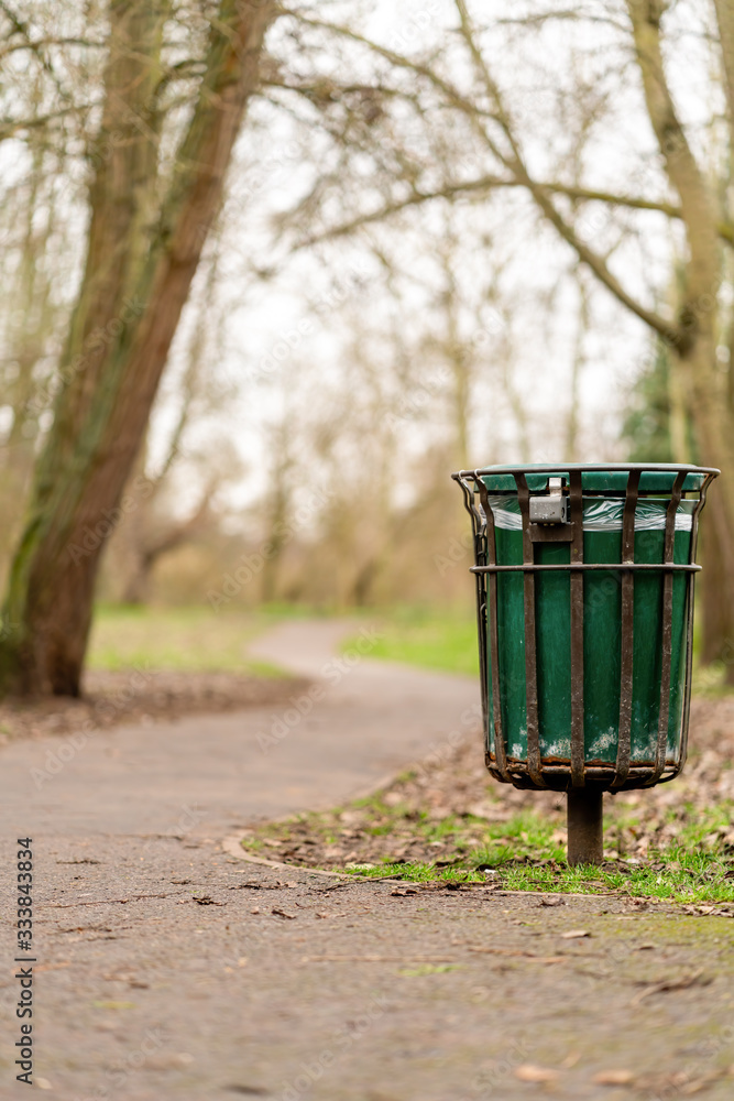Fototapeta premium A bin standing beside a path in a park in Twickenham, West London, England