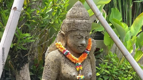 slow moving panning  Goddess Balinese statue with a garland of Marigolds.   Saraswati sculpture.  photo