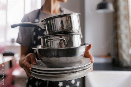 girl in an apron holds dishes, pots and kitchen utensils