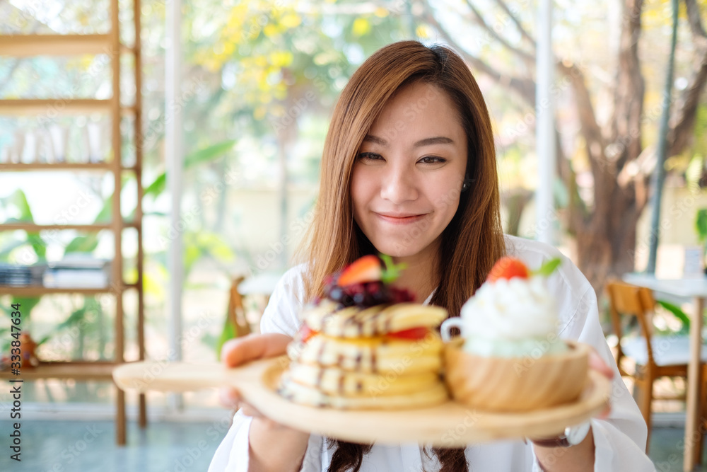 A beautiful asian woman holding and showing a plate of pancakes with ice cream and whipped cream in cafe