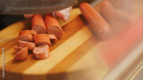 worker in gloves cuts fresh sausages with knife on board photo