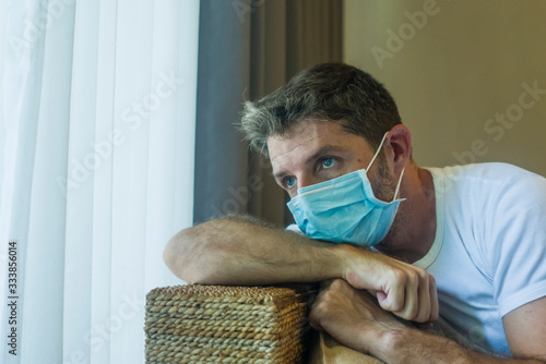 covid-19 virus lockdown - sad and worried man in medical mask thinking and feeling scared in quarantine following stay at home instructions to contain virus pandemic photo