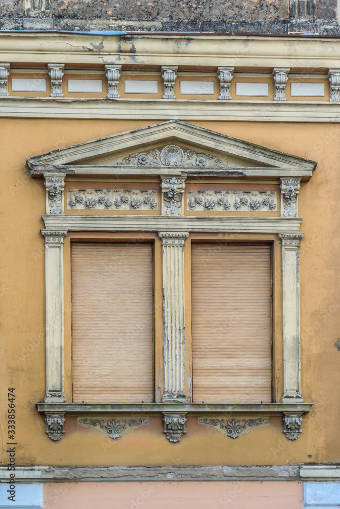 Classicism window on the yellow facade. Beautiful ornamented window of classicism style.