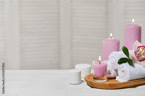 Spa products with aromatic candles, orchid flower and towel on white wooden table. Beauty spa treatment and relax concept. copy space