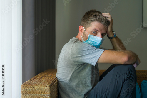 covid-19 virus lockdown - sad and worried man in medical mask thinking and feeling scared in quarantine following stay at home instructions to contain virus pandemic photo