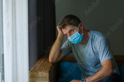 covid-19 virus lockdown - sad and worried man in medical mask thinking and feeling scared in quarantine following stay at home instructions to contain virus pandemic photo