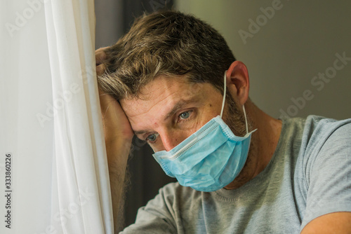 covid-19 virus lockdown - sad and worried man in medical mask thinking and feeling scared in quarantine following stay at home instructions to contain virus pandemic photo