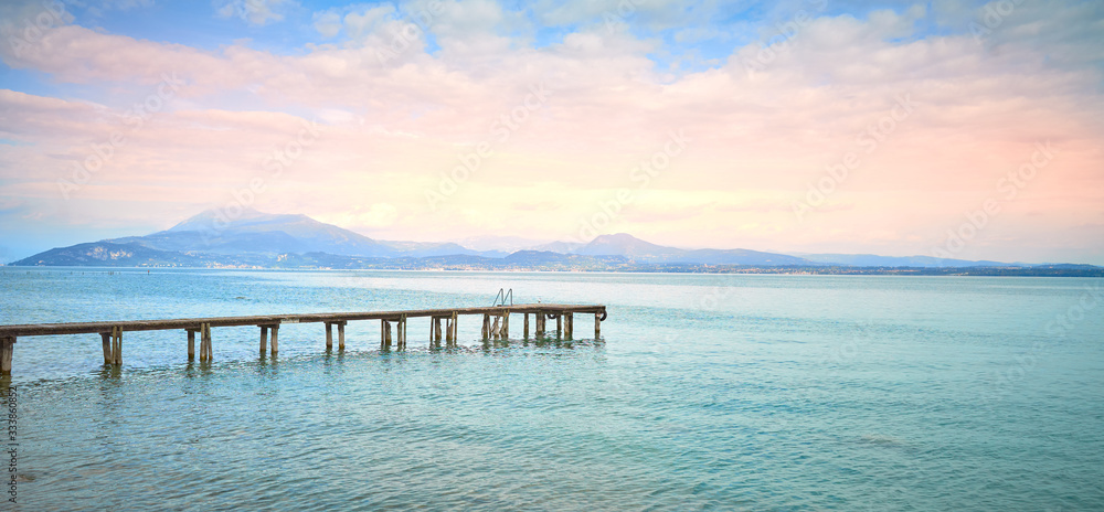 Wooden Pier at Lake Garda under dramatic Sky with beautiful light in the early mornung hours