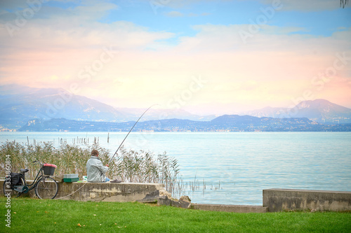 Retired man sitting in Sirmione at Lake Garda with his fishing rod, watching beautiful morning sky