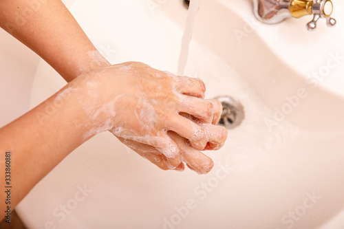 Young woman washing hands in modern sink with soap and lathering suds to protect against the coronavirus or covid 19. Bathroom hygiene concept.