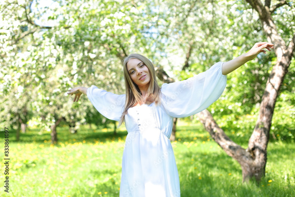 Happy blonde woman on a background of blooming spring garden with her hands raised to the sky Happy blonde woman on a background of blooming spring garden with her hands raised to the sky