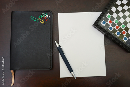 Top view of a pen on a piece of blank paper  notebook and a checked board isolated on wooden background.  A from home and work life balance concept