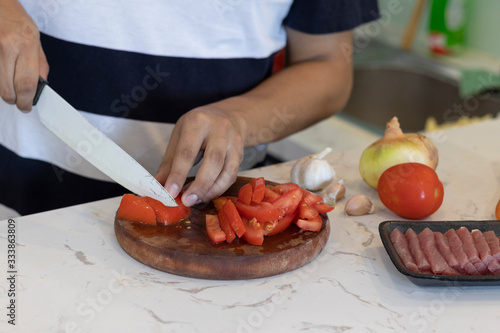 man cutting a tomato white a knife on a white kitchen table with vegetables in the background