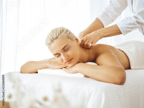 Beautiful blonde woman enjoying back massage with closed eyes. Spa salon concept