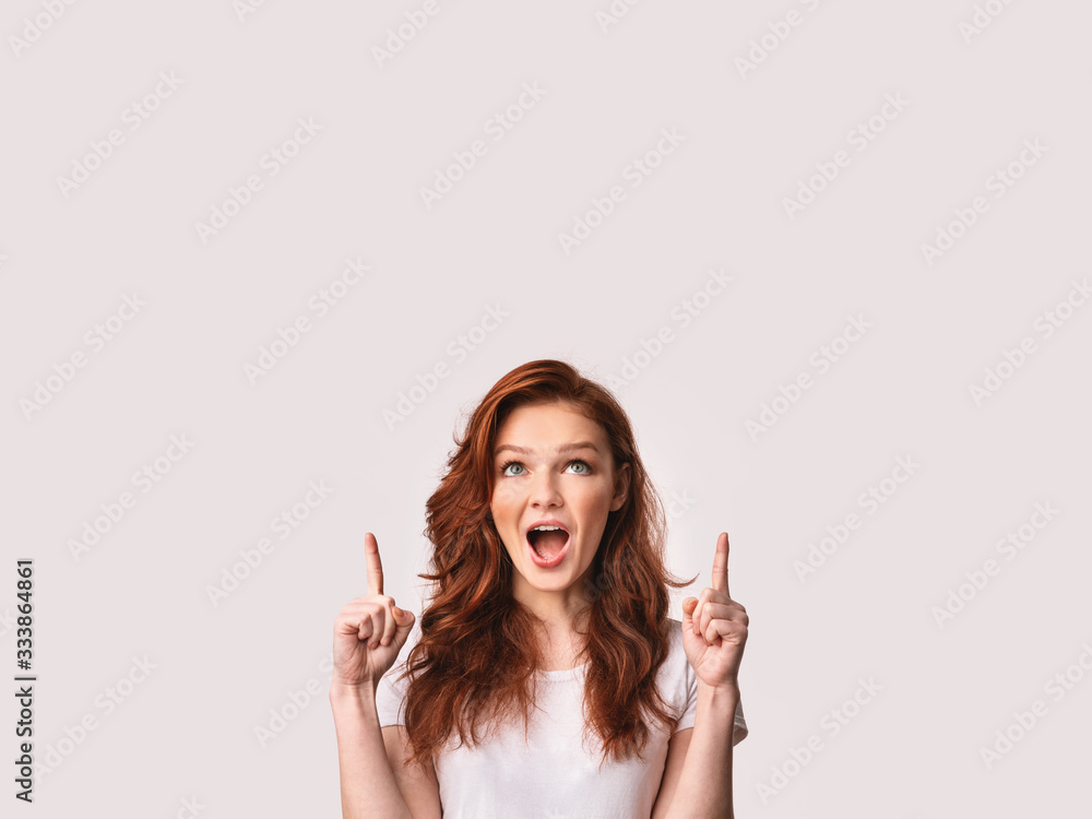 Girl Pointing Fingers Upward At Free Space Over White Background