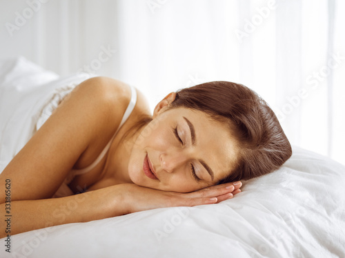 Beautiful young brunette woman sleeping while lying in bed comfortably and blissfully. Good morning concept