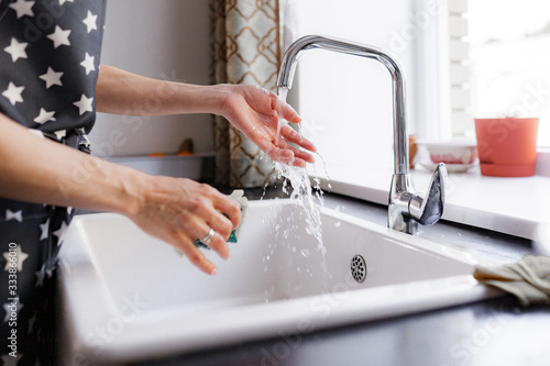 girl in an apron washes dishes in the kitchen, daylight.