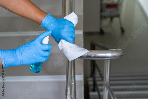 Close up of female hand using wet wipe and hand sanitizer spray to clean stainless steel staircase railing.Antiseptic,disinfection ,cleanliness and healthcare,anti virus concept.Anti bacterial and Cor