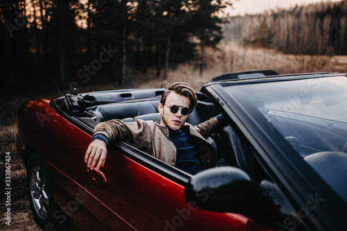 young male driver in sunglasses in a convertible in the summer at sunset. travel concept.