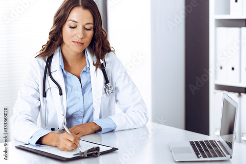 Doctor woman filling up medical form while sitting at the desk in hospital office. Physician at work. Medicine and health care concept