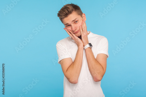 Portrait of lazy depressed young man in casual white t-shirt leaning on hands with bored tedious expression, feeling exhausted, indifferent to life. indoor studio shot isolated on blue background