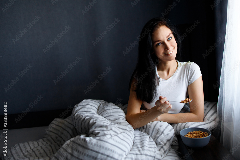 Breakfast woman with yoghurt cereal lying in bed eating a healthy snack with fruit and carefree smile Breakfast woman with yoghurt cereal lying in bed eating a healthy snack with fruit and carefree smile