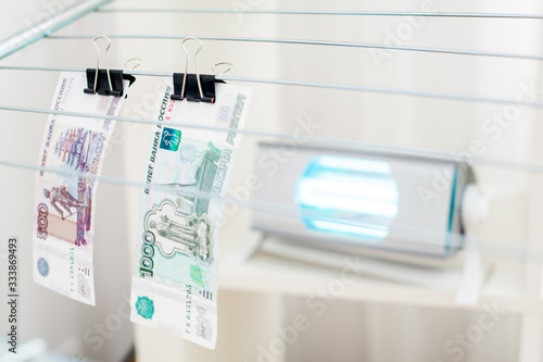 Fototapeta Naklejka Na Ścianę i Meble -  Sterilization of money by an ultraviolet lamp at home. Money is hung on clothespins and an ultraviolet lamp is directed at them.