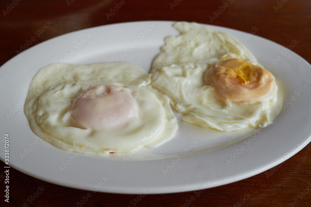 Two fried eggs for breakfast on a white plate on a wooden table.    