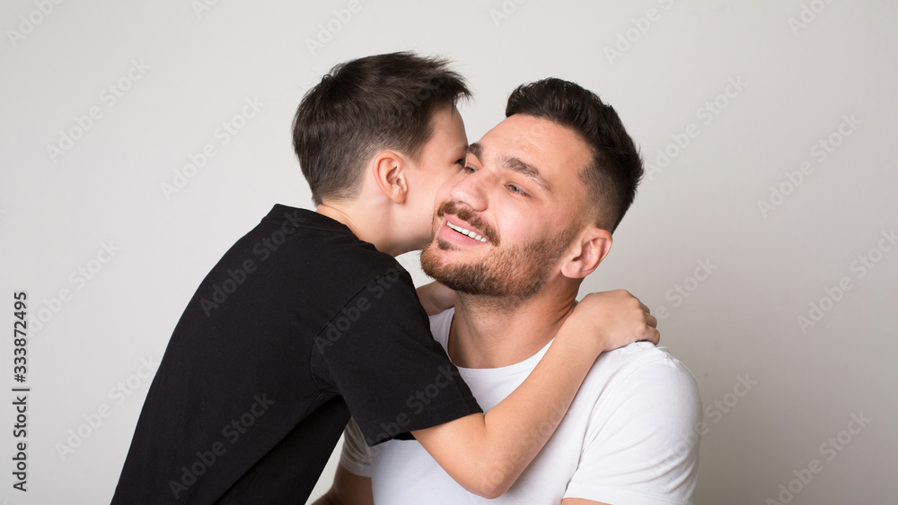 Cheerful boy hugging with his father, gray studio background Cheerful boy hugging with his father, gray studio background