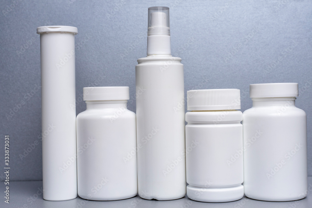 5 white jars for medicines and vitamins and dietary supplements without a name are on a gray shelf. 5 white jars for medicines and vitamins and dietary supplements without a name are on a gray shelf.