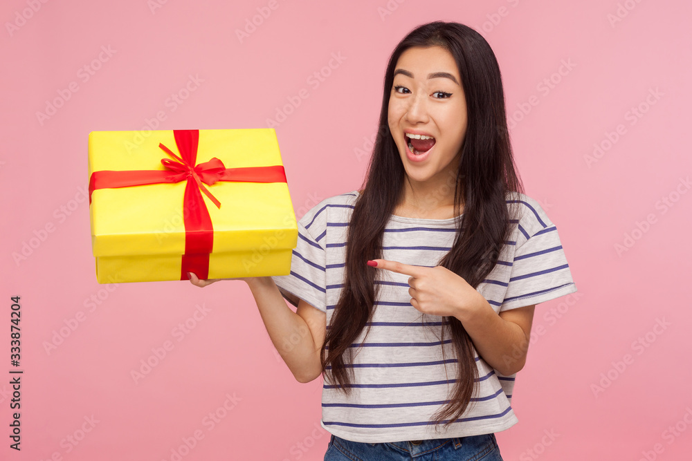 Awesome birthday present! Amazed satisfied pretty girl with brunette hair in striped t-shirt pointing at gift box and looking with surprised expression. indoor studio shot isolated on pink background Awesome birthday present! Amazed satisfied pretty girl with brunette hair in striped t-shirt pointing at gift box and looking with surprised expression. indoor studio shot isolated on pink background