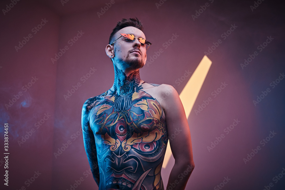 Self-assured male model posing in a neon studio with a half-naked body wearing fire-shaped sunglasses and tattooed in a japanese irezumi style, looking cool and relaxed.