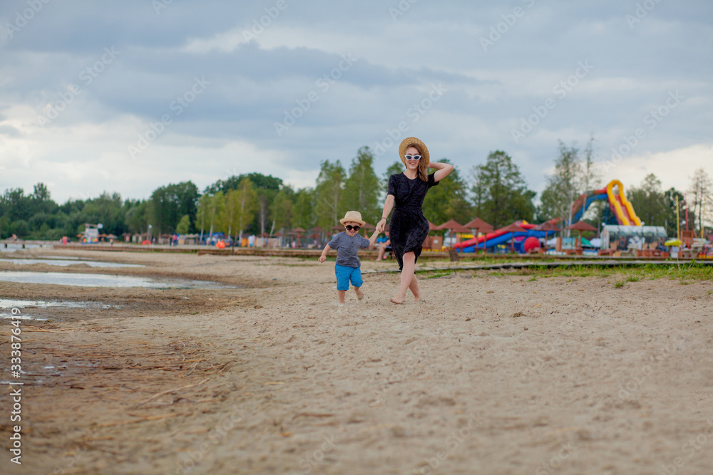 A young beautiful girl runs along a sandy beach in the sea with her son A young beautiful girl runs along a sandy beach in the sea with her son