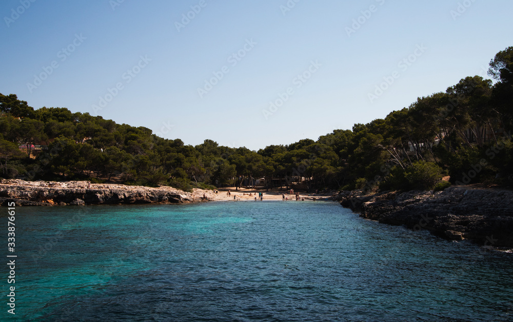 Blick in türkis blaue Bucht mit badenden Urlaubern umrahmt von Felsen und Sandstrand