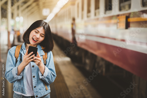 happy woman traveler with smartphone at train station platform