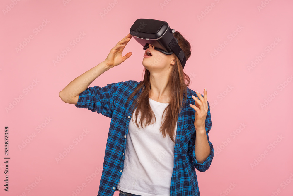 Portrait of gamer girl in checkered shirt wearing vr headset, playing virtual reality game with amazed facial expression, surprised by innovative technology. studio shot isolated on pink background Portrait of gamer girl in checkered shirt wearing vr headset, playing virtual reality game with amazed facial expression, surprised by innovative technology. studio shot isolated on pink background