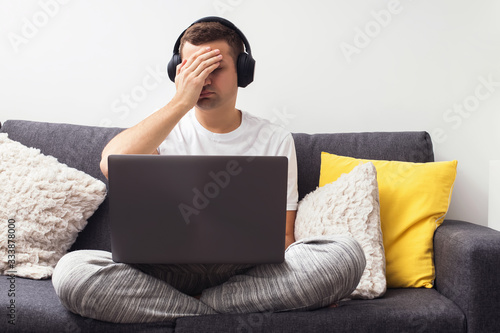 Young frustrated man sitting on the couch with laptop.