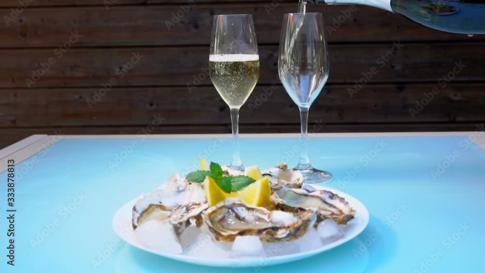 Champagne is poured into the glass next to the white plate with delicious fresh open oysters on the ice Champagne is poured into the glass next to the white plate with delicious fresh open oysters on the ice