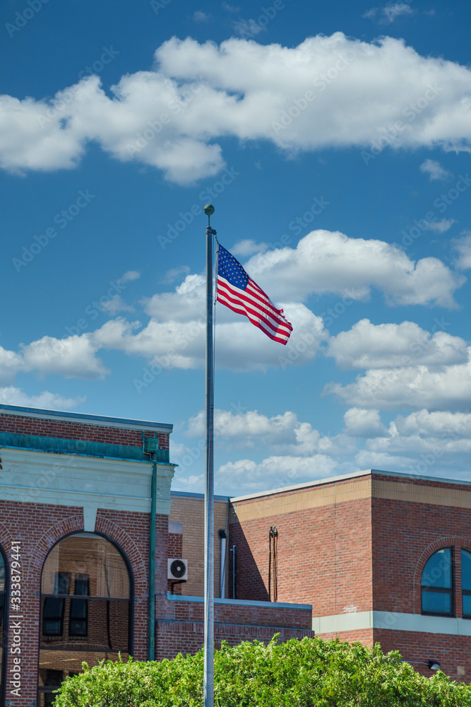 An American flag flying under blue skies in front of an old brick government building