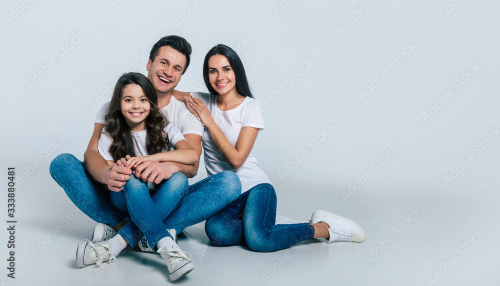 Happy beautiful young family in white t-shirts while they hugging each other isolated on a light background. Happy beautiful young family in white t-shirts while they hugging each other isolated on a light background.