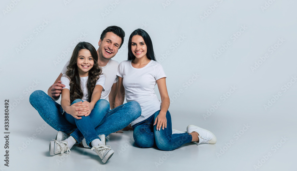 Happy beautiful young family in white t-shirts while they hugging each other isolated on a light background.