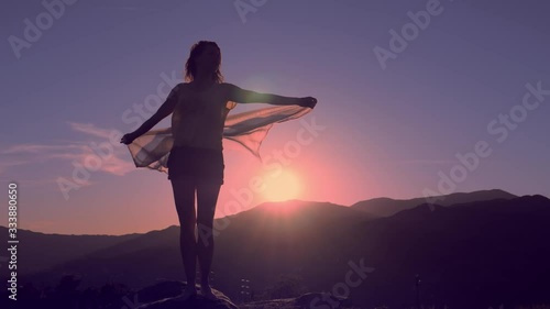 Young woman with hands up holding scarf in wind on mountain landscape