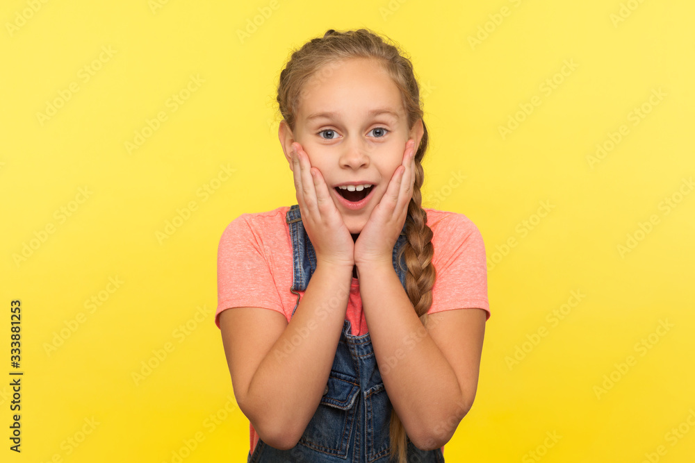 Awesome unexpected event. Portrait of astonished little girl touching face in surprise, expressing amazement, child shocked by sudden crazy news. indoor studio shot isolated on yellow background Awesome unexpected event. Portrait of astonished little girl touching face in surprise, expressing amazement, child shocked by sudden crazy news. indoor studio shot isolated on yellow background