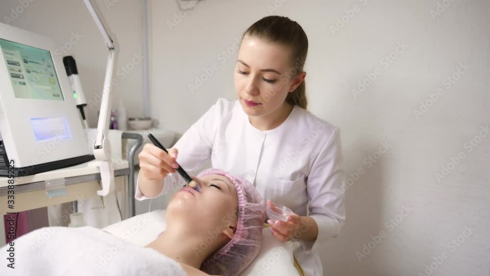 girl doctor cosmetologist puts a special gel brush on the face before the anti aging procedure girl doctor cosmetologist puts a special gel brush on the face before the anti aging procedure