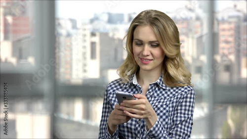 Young cheerful woman in office texting on phone. Portraing of a positive lady using her mobile phone in bright office. photo