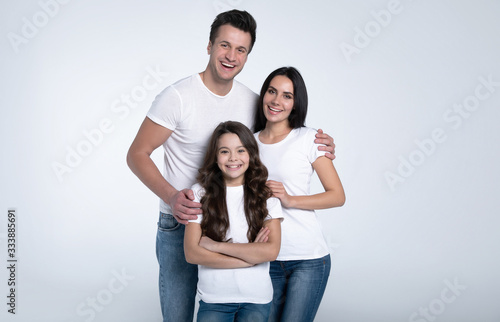 Happy beautiful young family in white t-shirts while they hugging each other isolated on a light background.