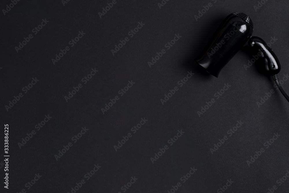 Naklejka premium Black electrical hand-held hair dryer for hair salon or barber shop on the black background with copy space