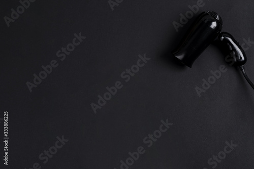 Black electrical hand-held hair dryer for hair salon or barber shop on the black background with copy space